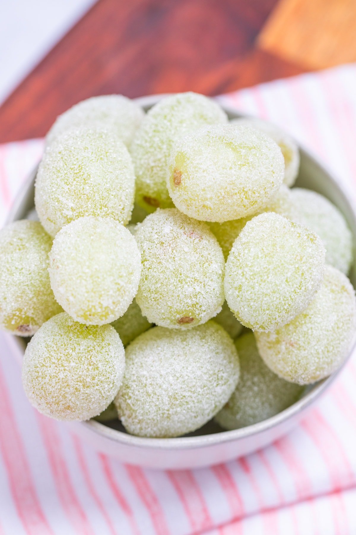 A bowl of sugared grapes on a tea towel on a wooden cutting board.
