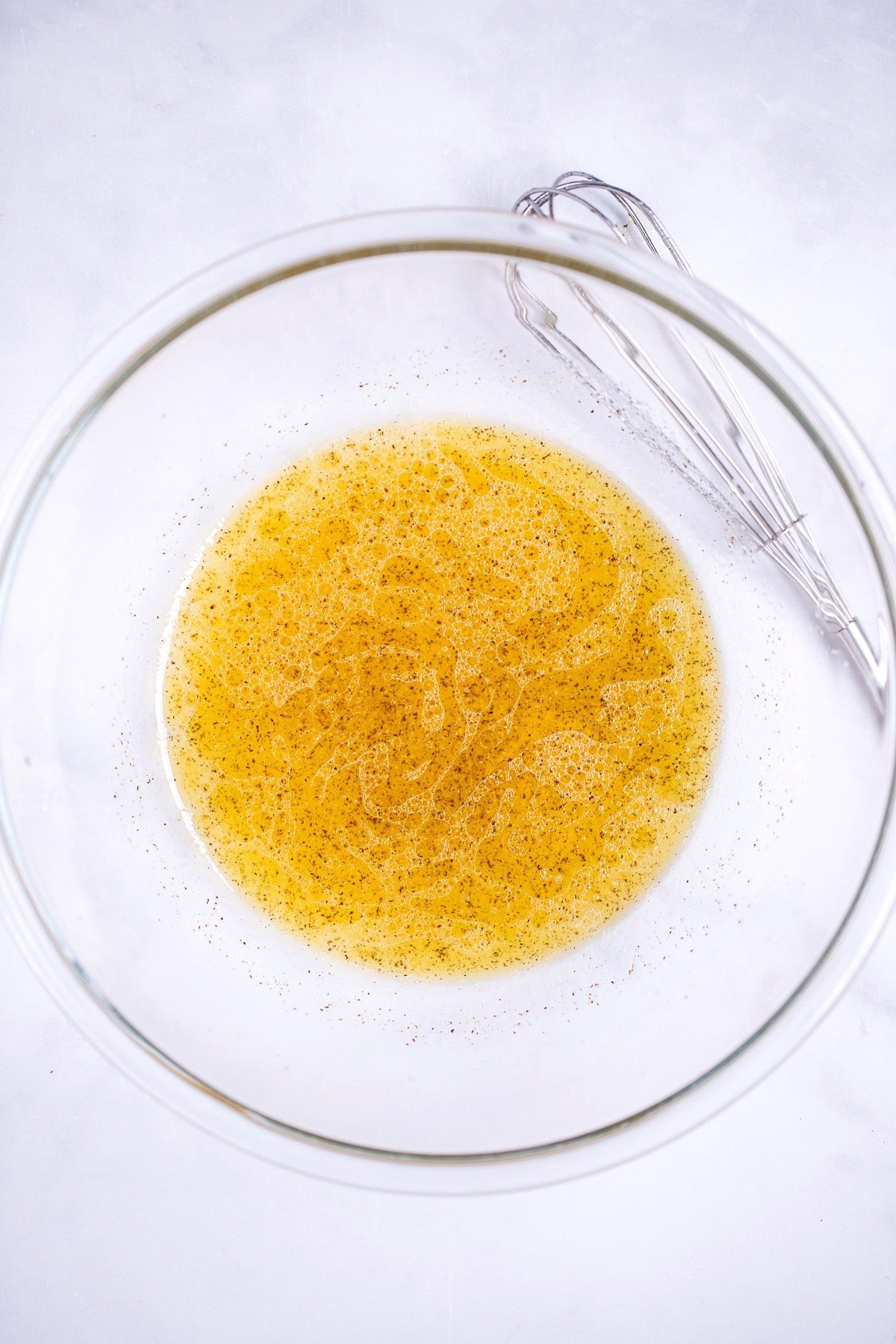 A glass bowl on a table full of lime vinaigrette dressing, in front of a whisk resting on the table.