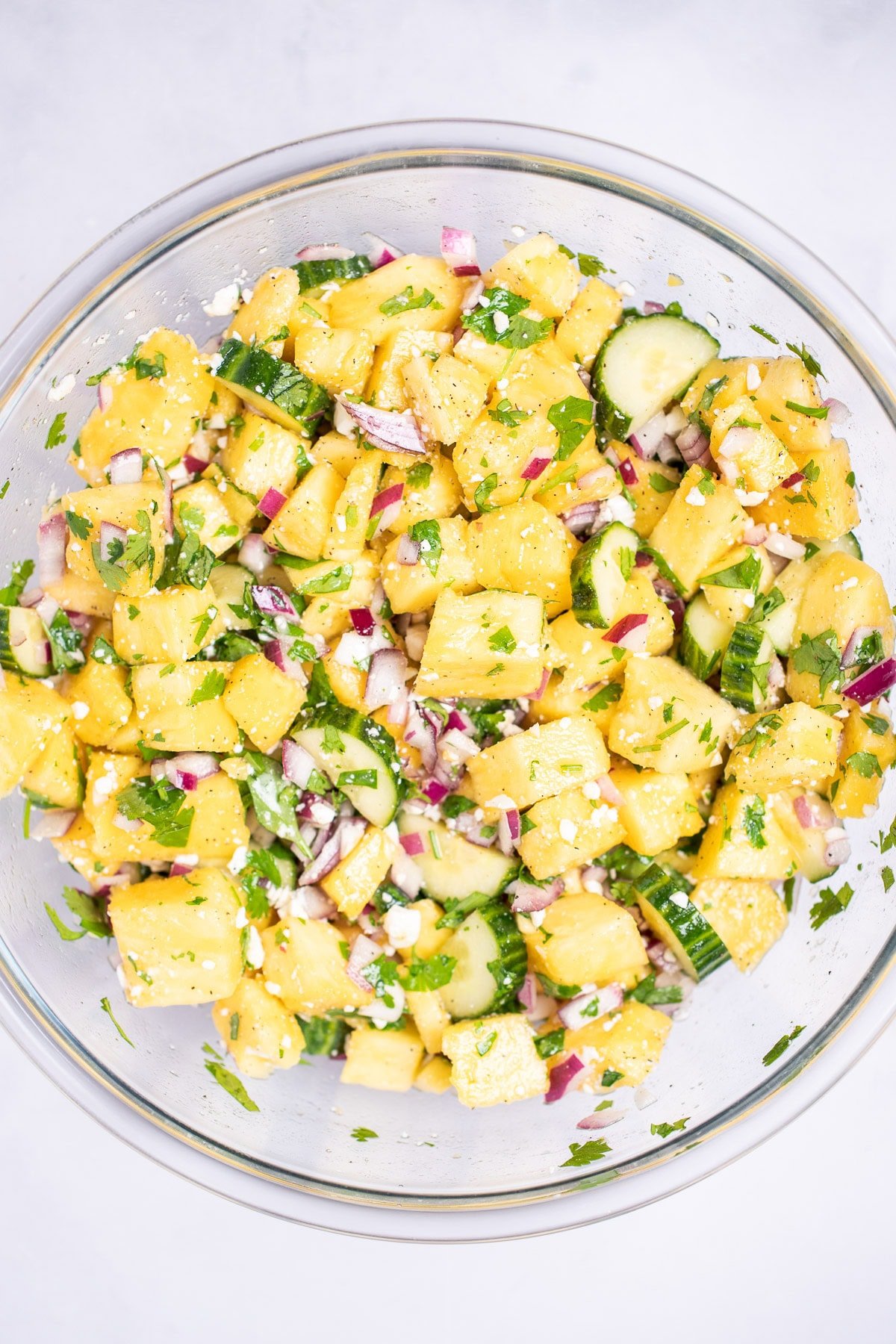 A glass bowl with pineapple cucumber salad after just being mixed.