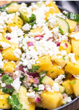 Pinterest pin with a bowl of pineapple cucumber salad topped with feta cheese sitting on a wooden cutting board.