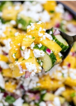 Pinterest pin with a bowl of pineapple cucumber salad topped with feta cheese with a spoon lifting some up.