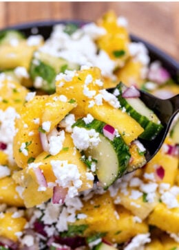 Pinterest pin with a bowl of pineapple cucumber salad topped with feta cheese with a spoon lifting some up.
