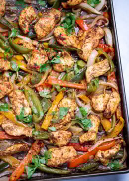 A sheet pan lined with parchment paper with cooked chicken and peppers topped with fresh cilantro.