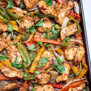 A sheet pan lined with parchment paper with cooked chicken and peppers topped with fresh cilantro.