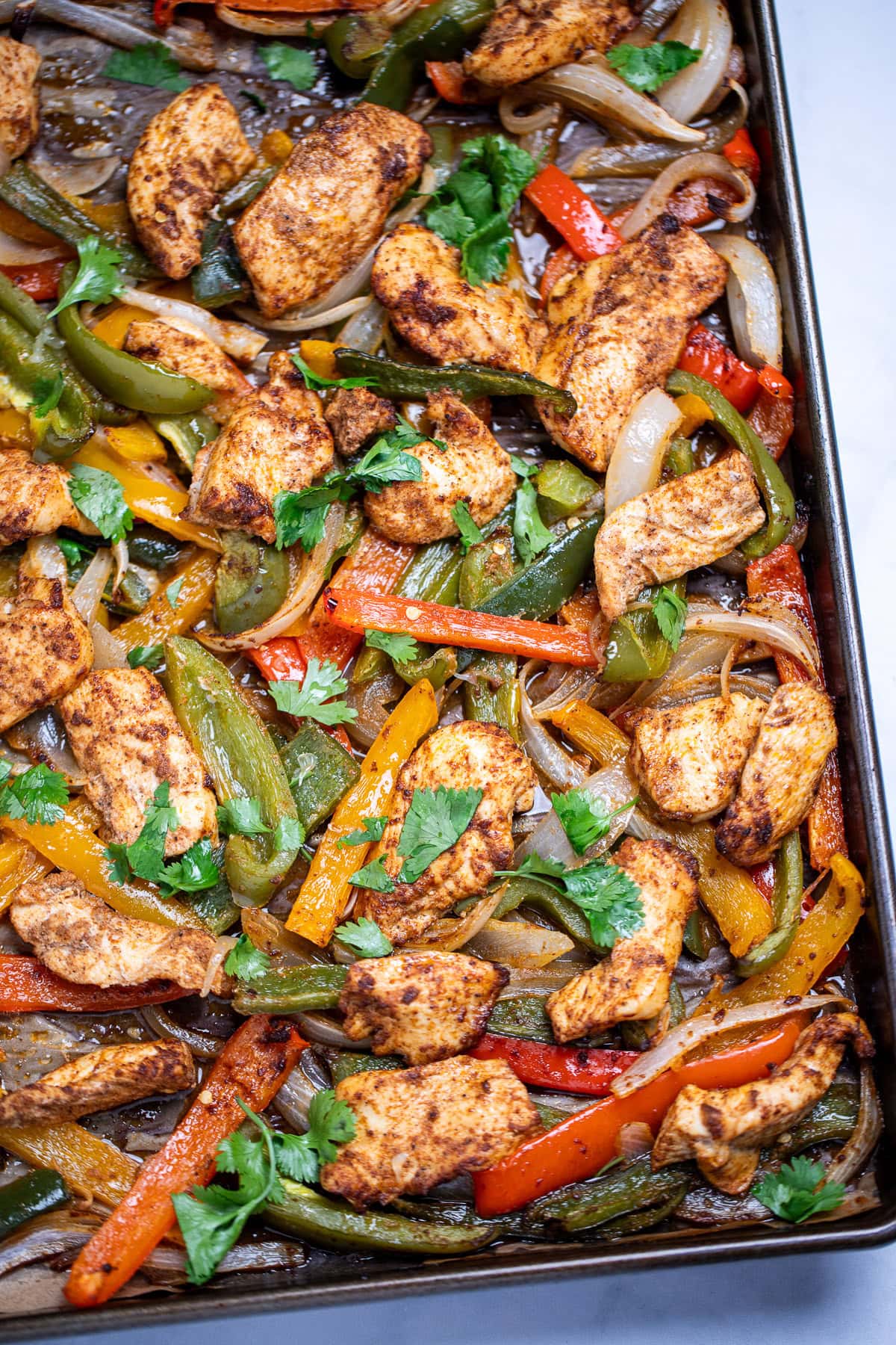 A sheet pan lined with parchment paper with cooked chicken and peppers topped with fresh cilantro.