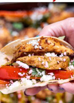 Pinterest pin with a hand holding a corn tortilla with fajita chicken, bell peppers, and cheese.