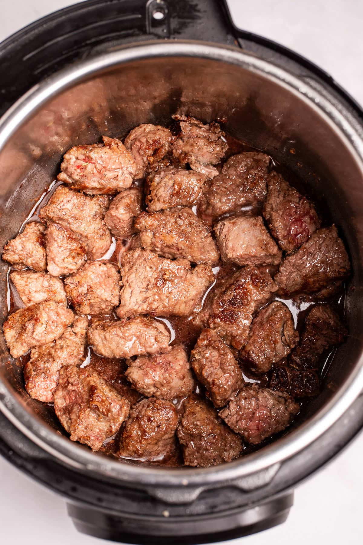 An instant pot with seared beef in a wine reduction.