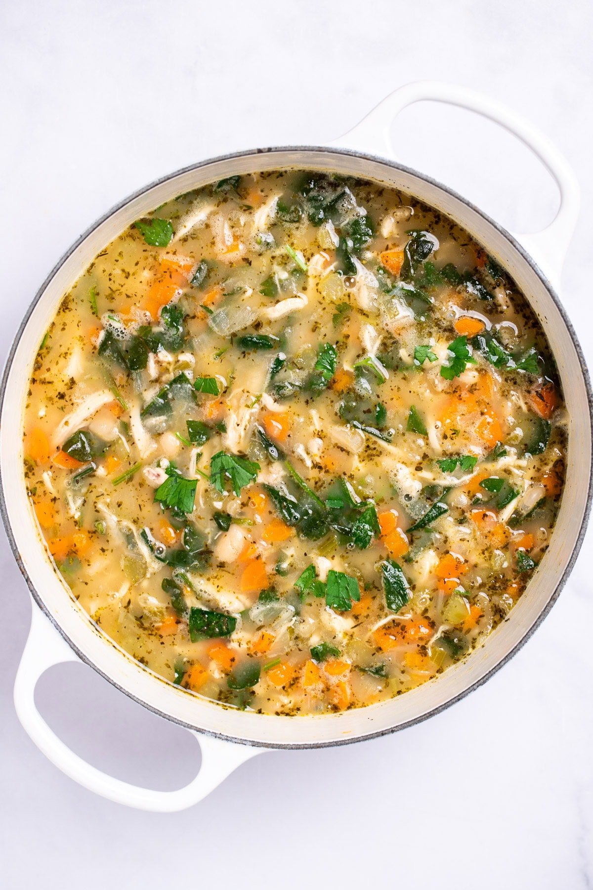 A dutch oven full of white bean chicken soup on a table.