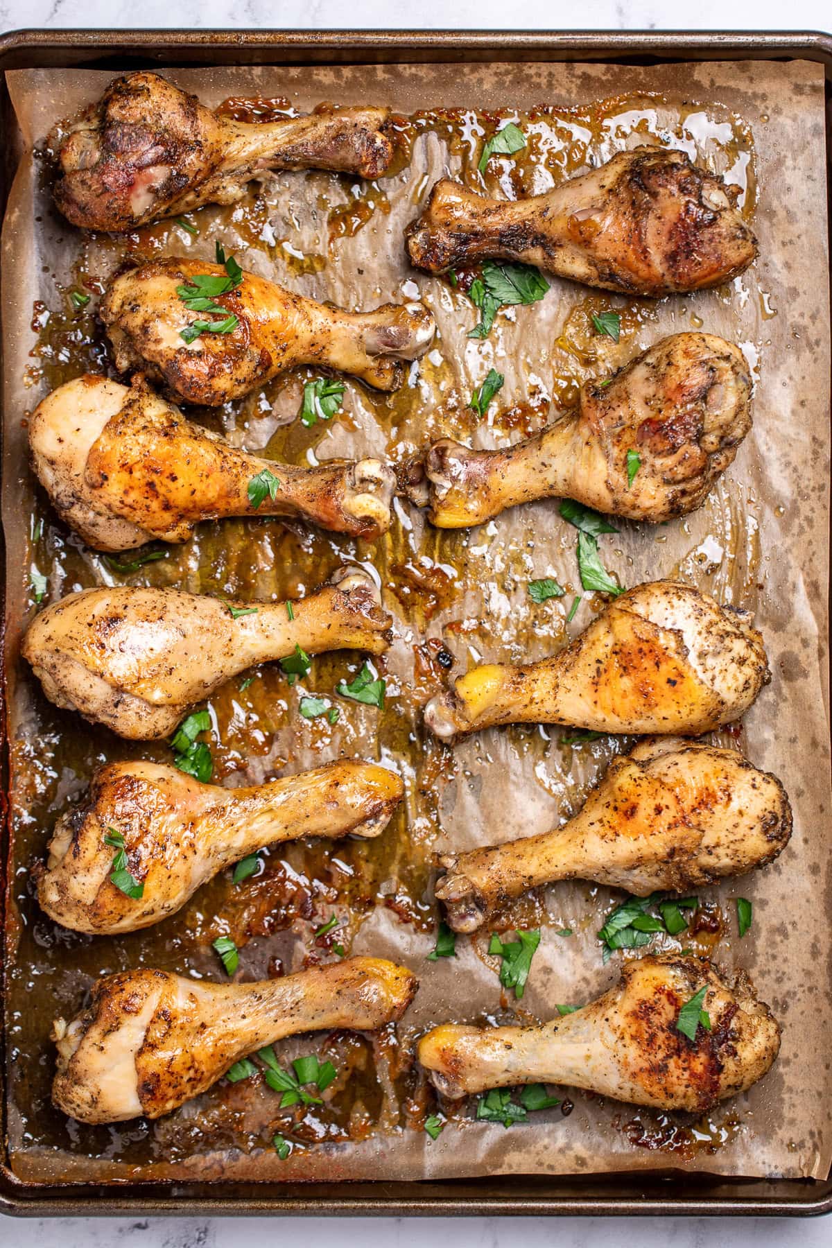 A sheet pan lined with parchment paper, with baked chicken legs in two rows on the pan, topped with fresh parsley.