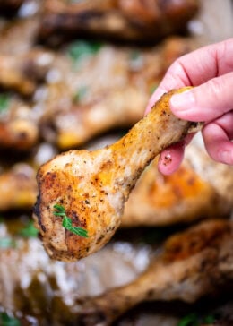 A hand holding a chicken drumstick that's been baked in the oven, topped with fresh parsley.