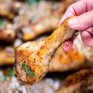 A hand holding a chicken drumstick that's been baked in the oven, topped with fresh parsley.