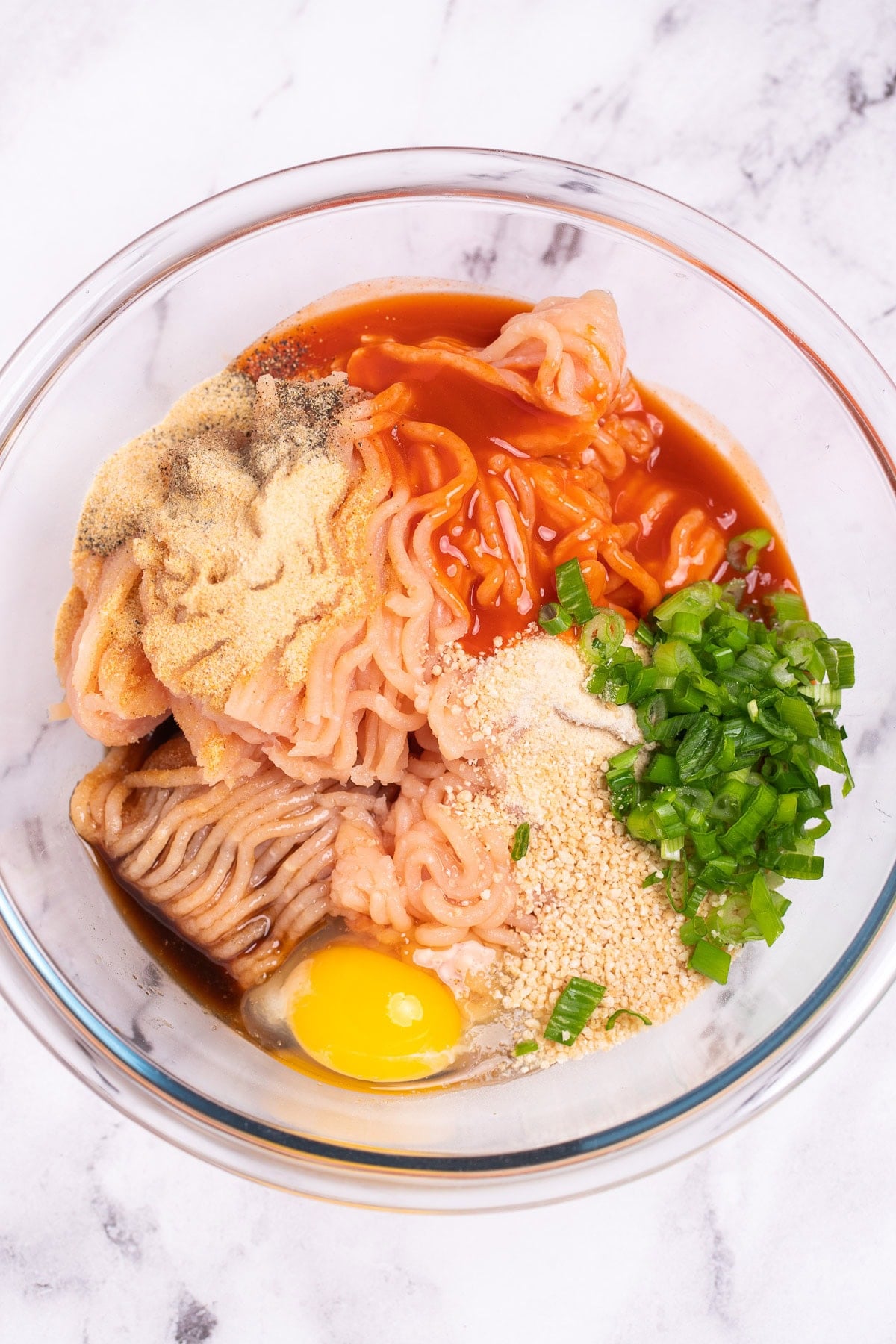 A mixing bowl on a table with individual ingredients for buffalo chicken burgers before being mixed together.