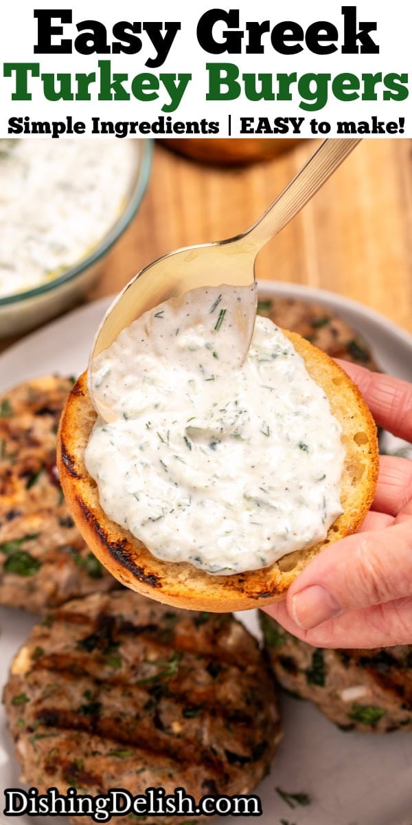 Pinterest pin with hands spooning tzatziki sauce onto a burger bun above a plate resting on a cutting board, with four grilled greek turkey burgers, next to red onion, a burger bun, and a bowl of tzatziki on the board.