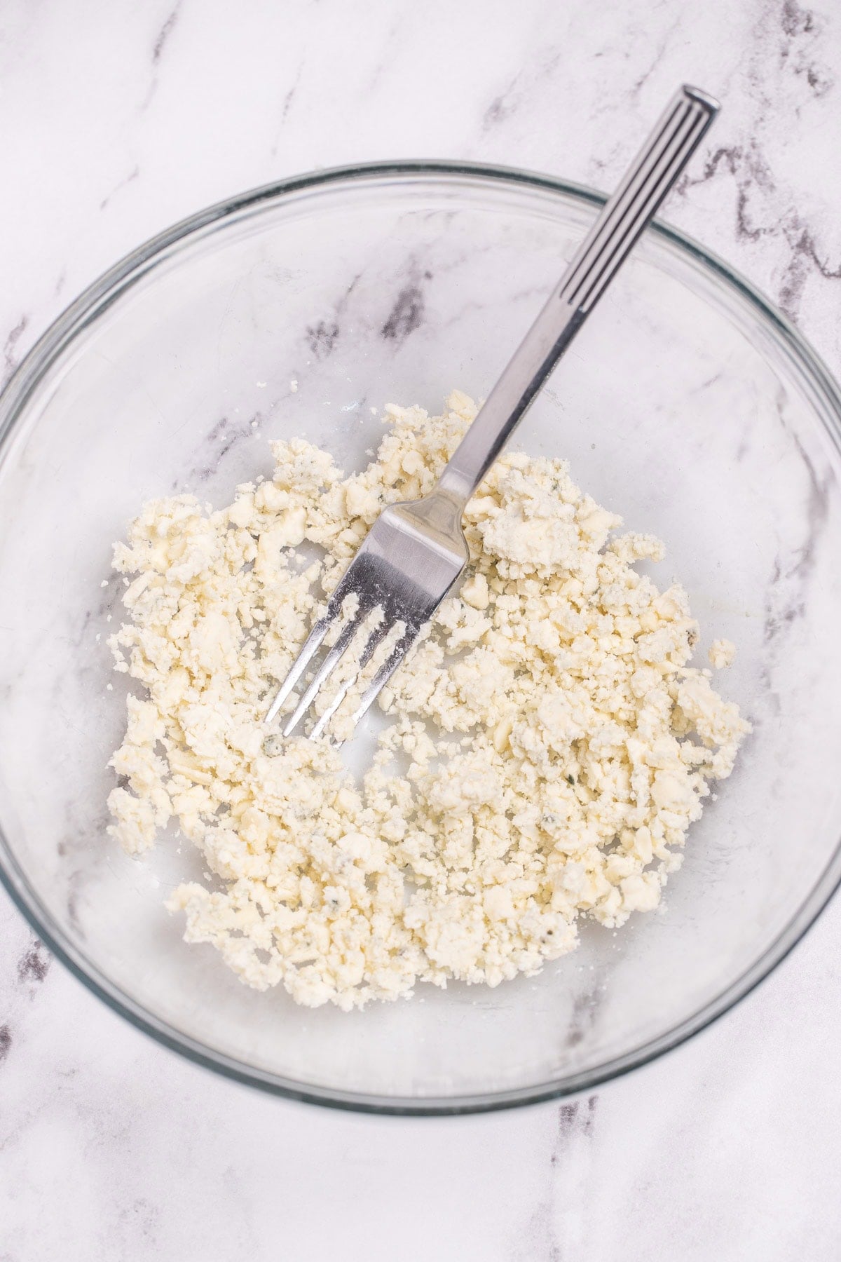 A glass bowl with blue cheese crumbles being broken up by a fork.