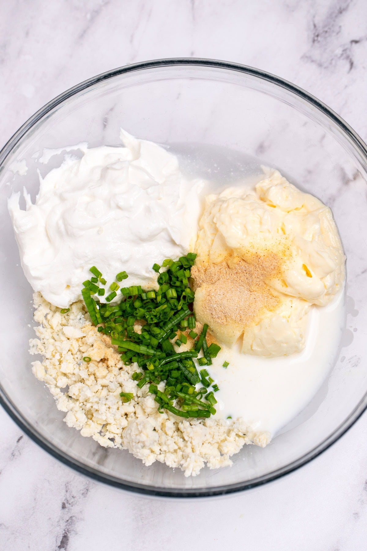 A glass bowl with each ingredient for blue cheese dressing before being mixed together.