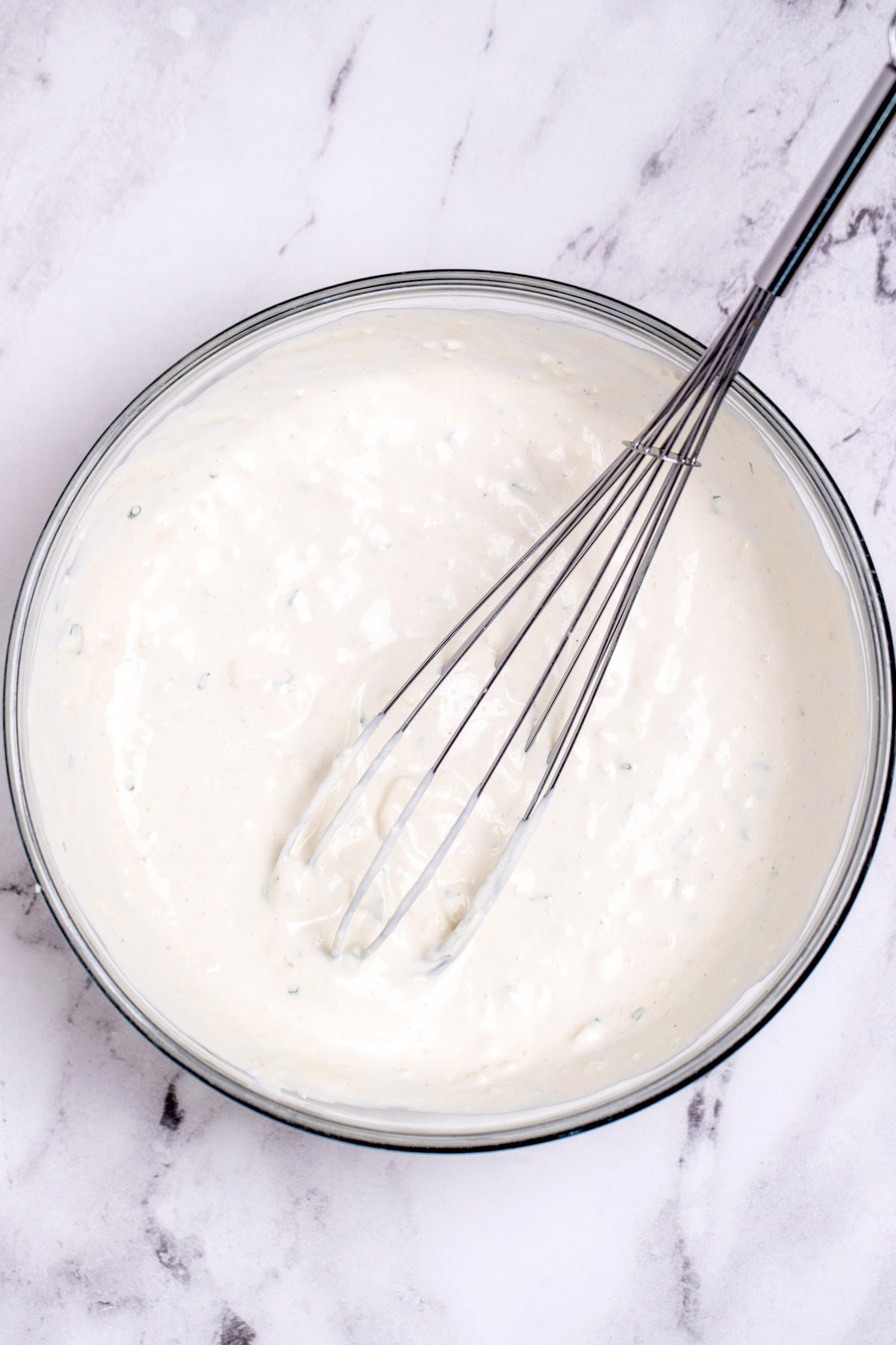 A mixing bowl on a table with blue cheese dressing and a whisk resting in it.