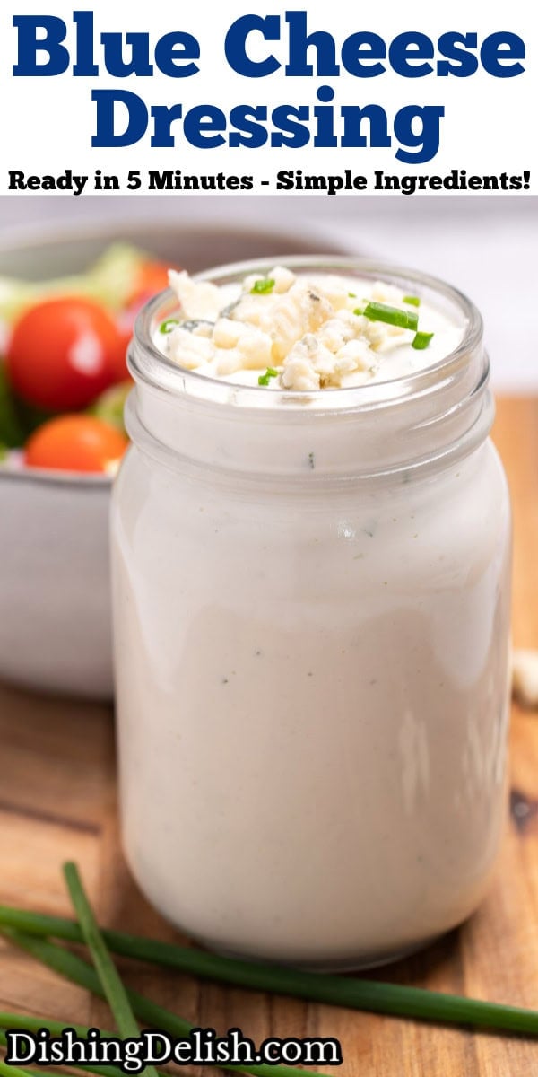 Pinterest pin with a mason jar of homemade blue cheese dressing resting on a cutting board with fresh chives and blue cheese crumbles around it, and a bowl of salad in the background.