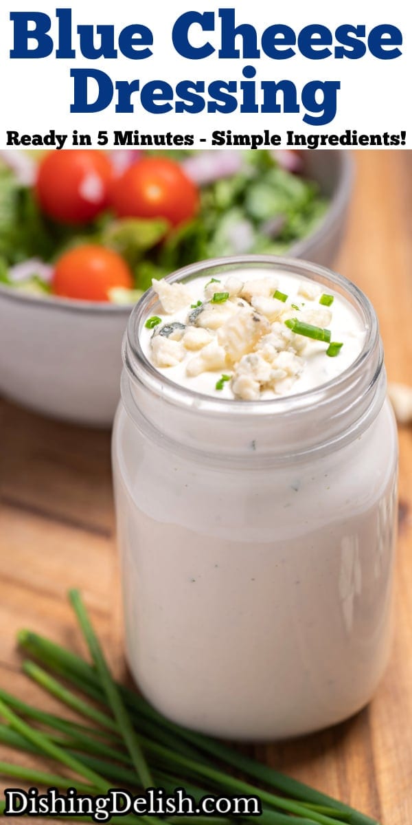 Pinterest pin with a mason jar of homemade blue cheese dressing resting on a cutting board with fresh chives and blue cheese crumbles around it, and a bowl of salad in the background.