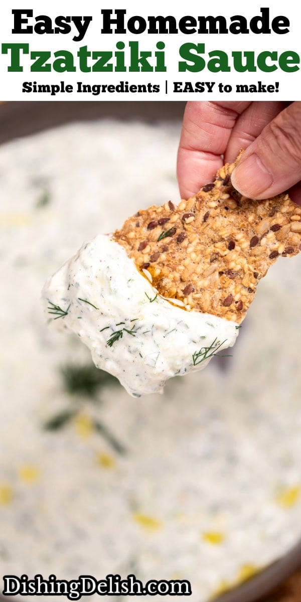 Pinterest pin with a bowl of homemade tzatziki sauce topped with fresh dill, on a cutting board with sliced cucumber, lemon, and gluten free crackers, with a hand holding a cracker lifting some tzatziki up.