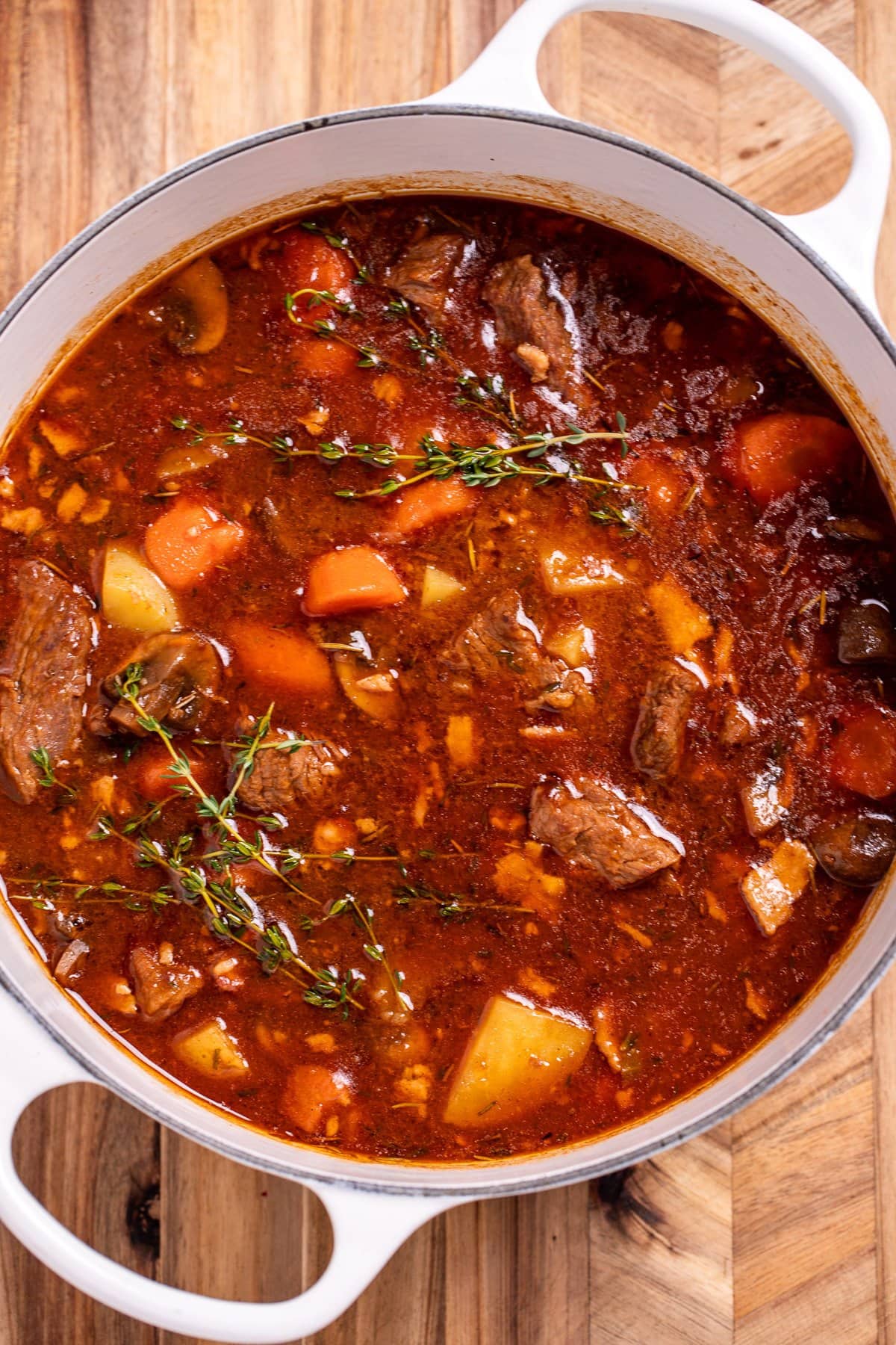 A dutch oven of Irish beef stew sitting on a cutting board, topped with fresh thyme.