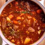 A dutch oven of Irish beef stew sitting on a cutting board, topped with fresh thyme.