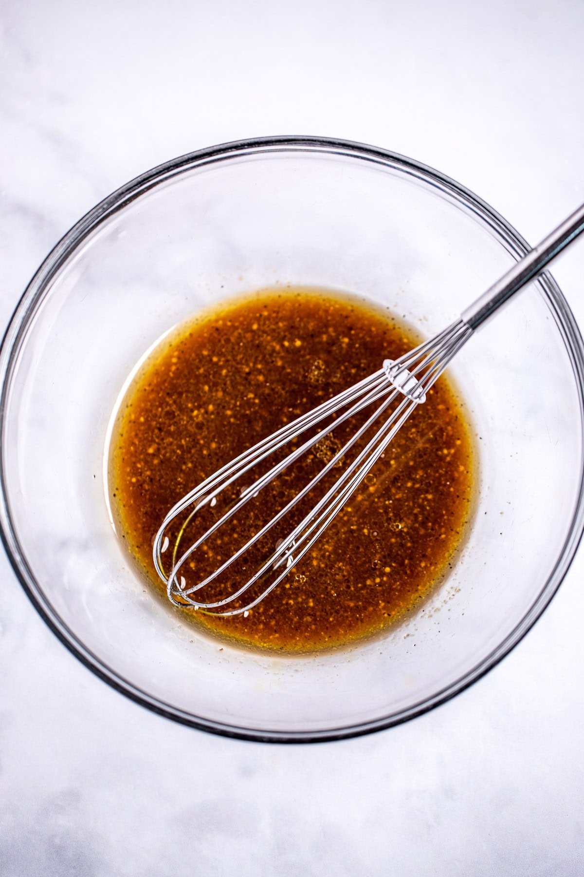 A glass bowl on a table, with balsamic vinaigrette and a whisk in it.