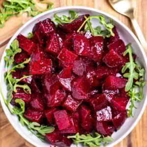 A bowl of roasted beet salad resting on arugula, on a cutting board next to a spoon.