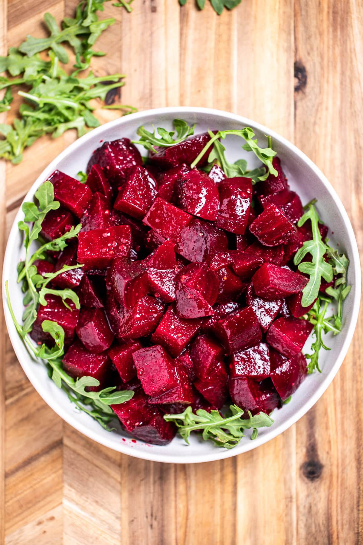 A bowl of roasted beet salad resting on arugula, on a cutting board.