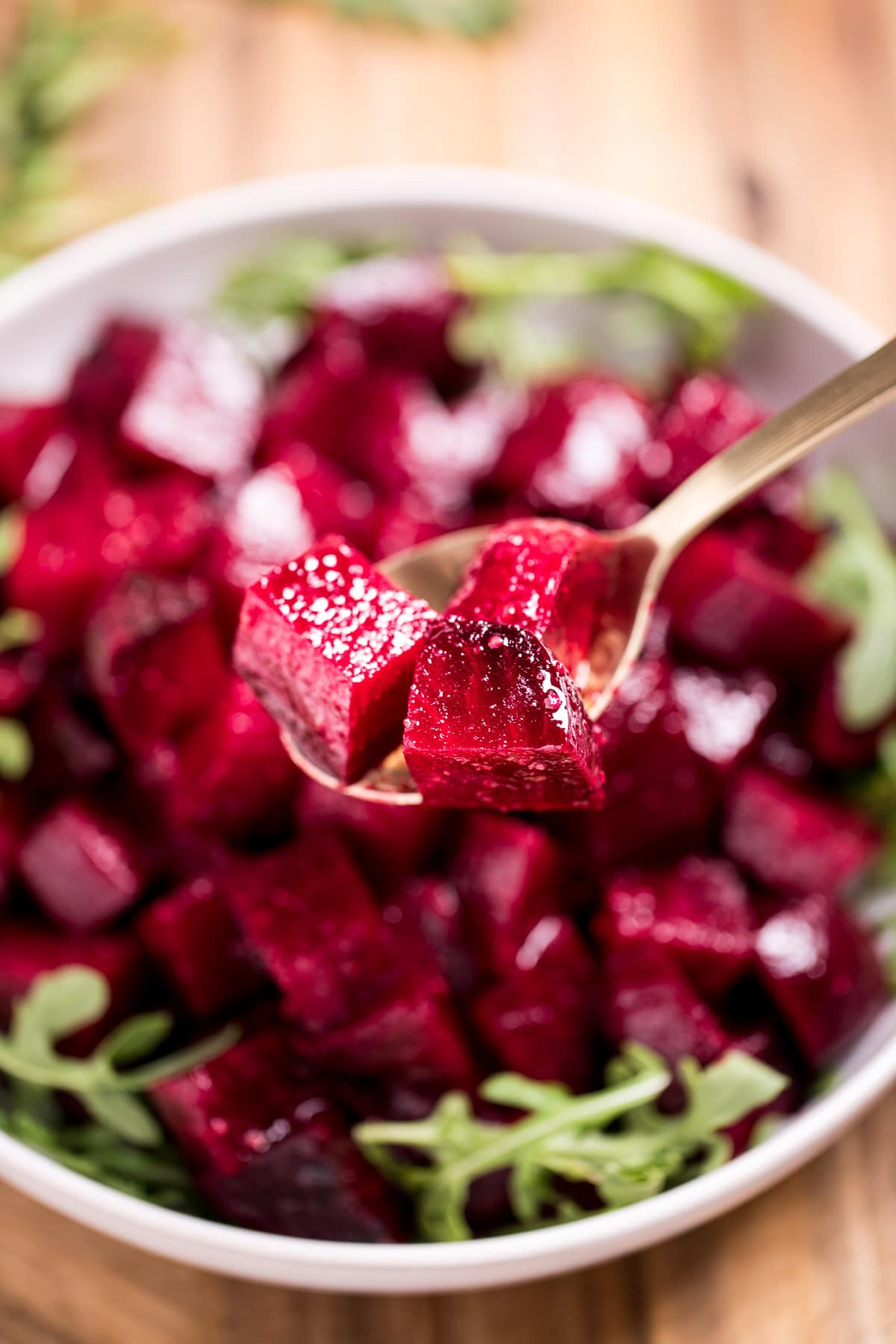 A bowl of roasted beet salad resting on arugula, on a cutting board, with a spoon lifting some beet pieces up.