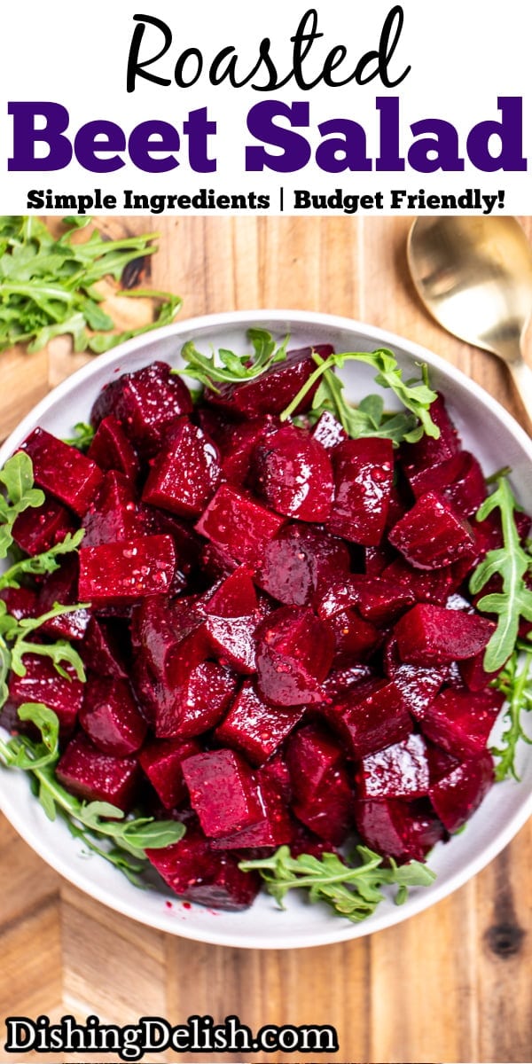 Pinterest pin with a bowl of roasted beet salad resting on arugula, on a cutting board, with a spoon next to it.