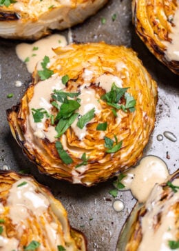 A sheet pan of roasted cabbage steaks topped with tahini dressing and chopped fresh parsley.