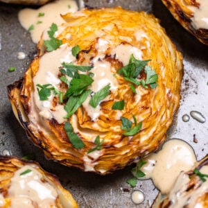 A sheet pan of roasted cabbage steaks topped with tahini dressing and chopped fresh parsley.