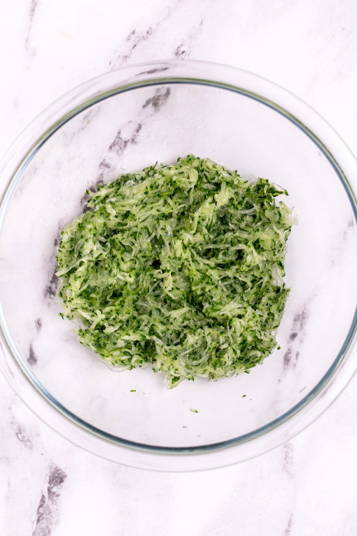 Glass bowl on a table with shredded cucumber in it.