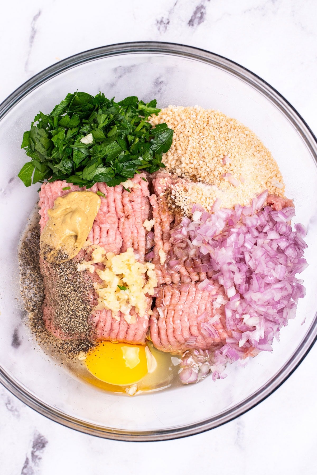 A glass bowl on a table with individual ingredients for homemade turkey burgers in it.