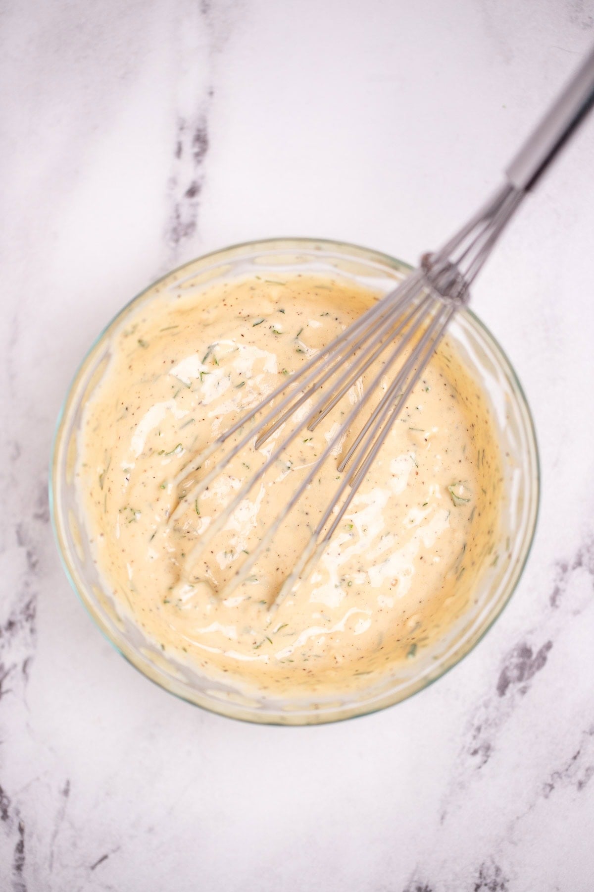 A glass bowl on a table with honey dijon sauce, and a whisk resting in the glass.