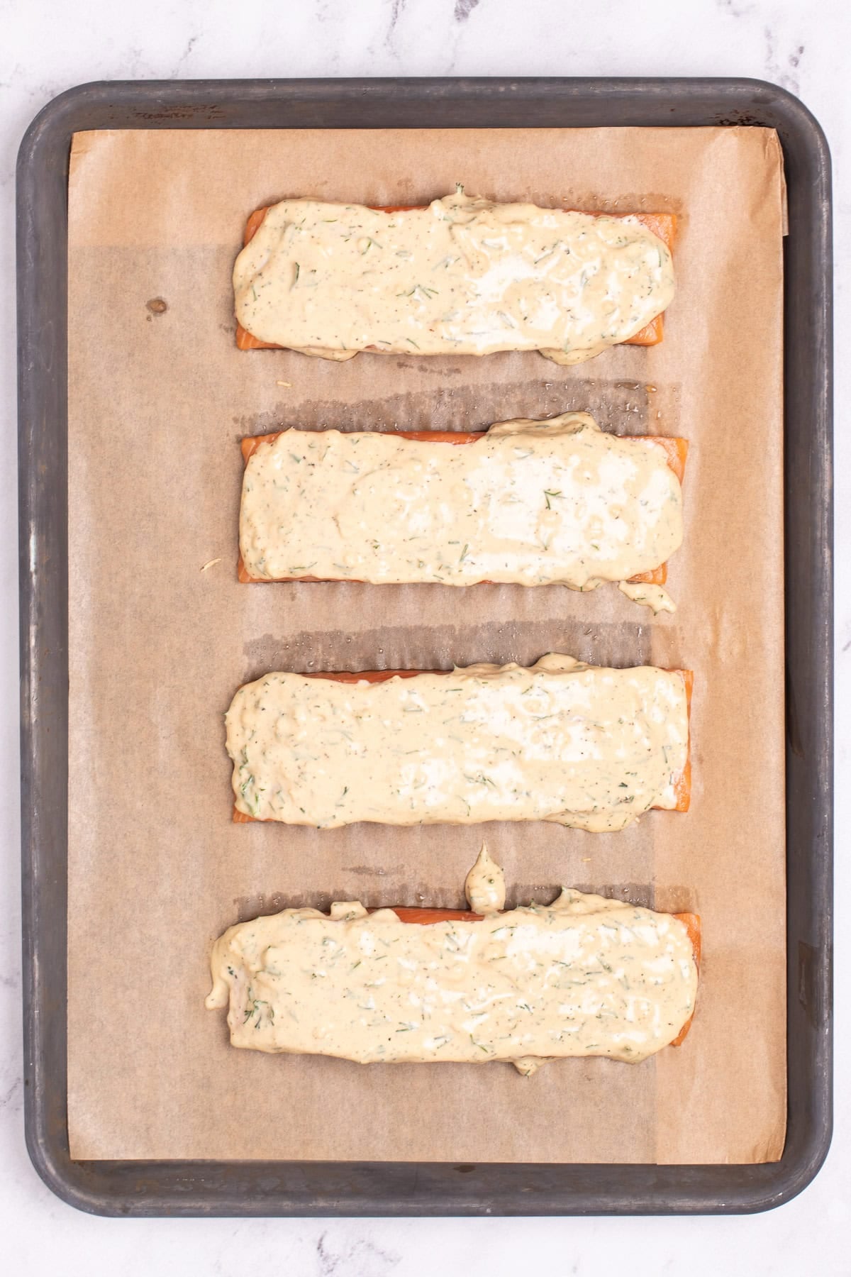 Four salmon fillets topped with honey dijon sauce, resting on a sheet pan lined with parchment paper, with some space between each piece.