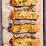 Four baked and broiled salmon fillets topped with honey dijon sauce, on a sheet pan lined with parchment paper, and topped with fresh chopped dill.