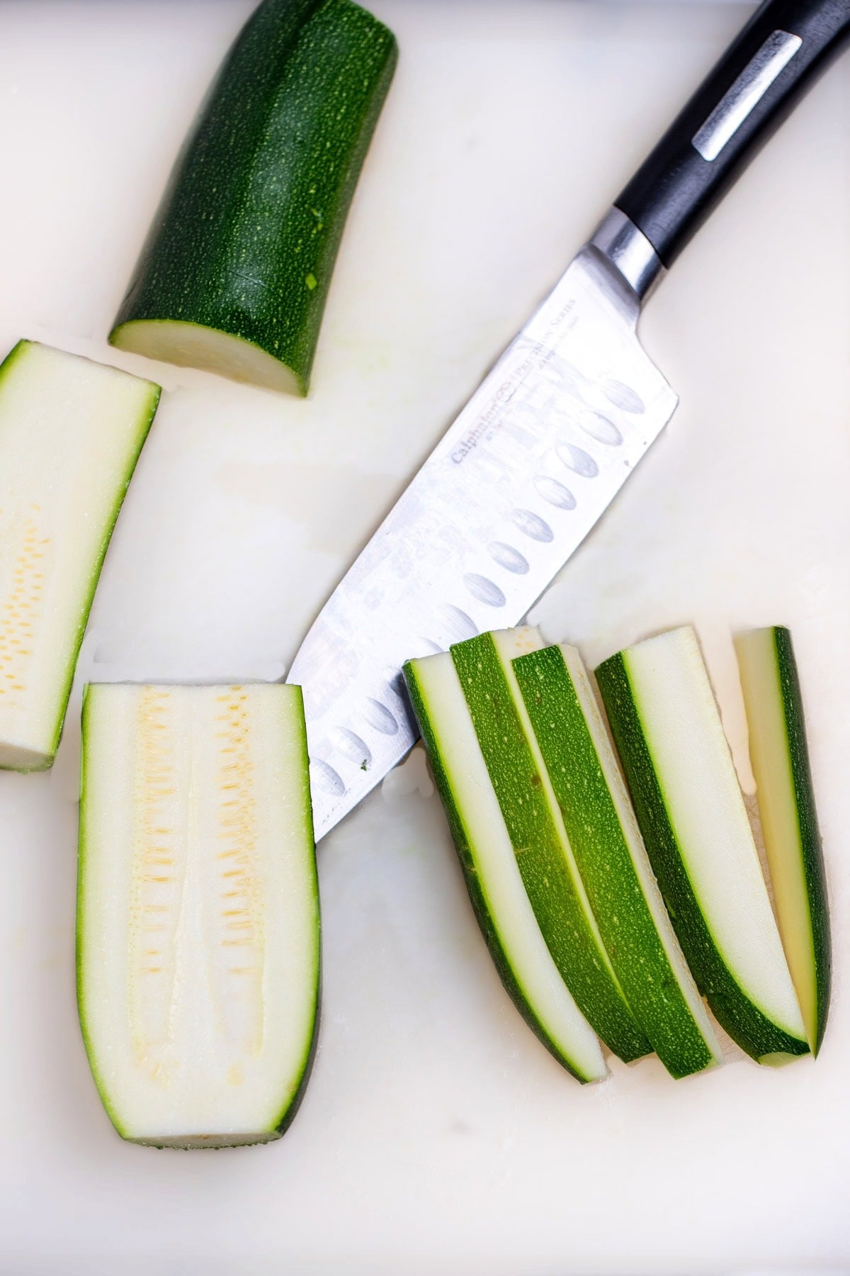 A cutting board with zucchini cut into pieces and a knife.