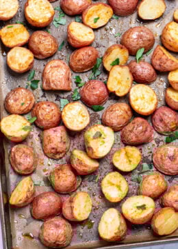 A sheet pan lined with parchment paper, with seasoned halved red potatoes after being roasted, topped with chopped fresh parsley.