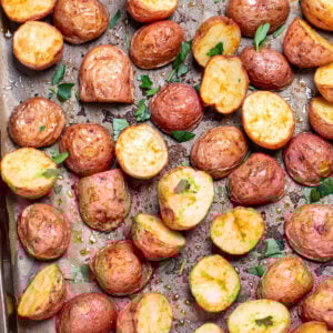A sheet pan lined with parchment paper, with seasoned halved red potatoes after being roasted, topped with chopped fresh parsley.