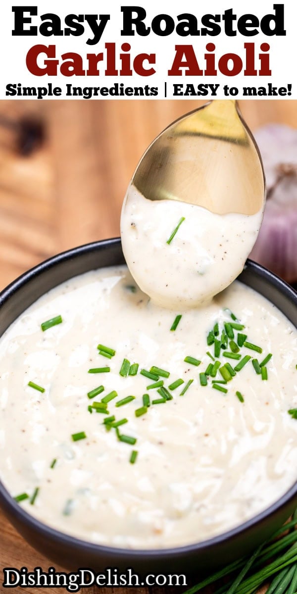 Pinterest pin with a small bowl of roasted garlic aioli topped with fresh chives, on a cutting board next to more chives and a bulb of garlic. A spoon is dipping into the sauce and lifting some up.