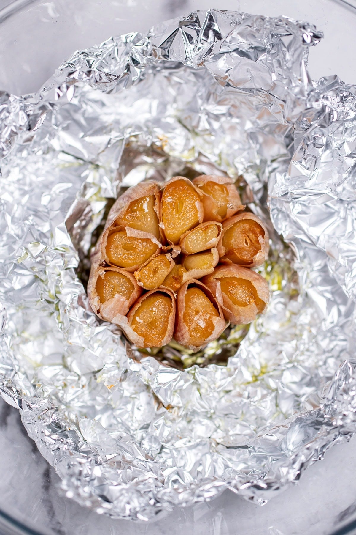 A roasted garlic bulb in a ball of tinfoil, with the top cut off, right after being roasted.