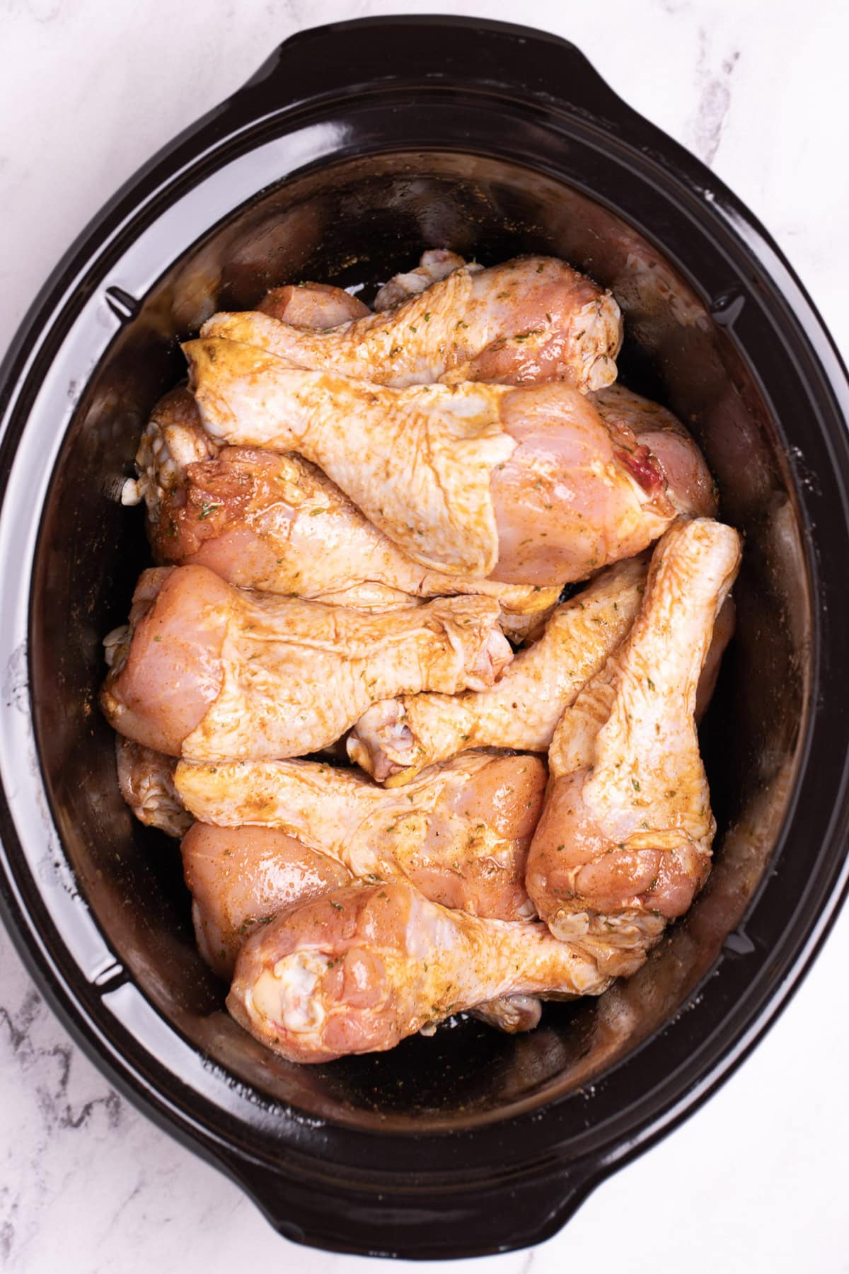 A slow cooker full of seasoned raw chicken drumsticks.