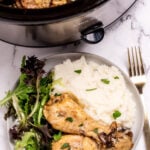 A plate with two chicken legs next to salad and mashed potatoes, in front of a slow cooker.