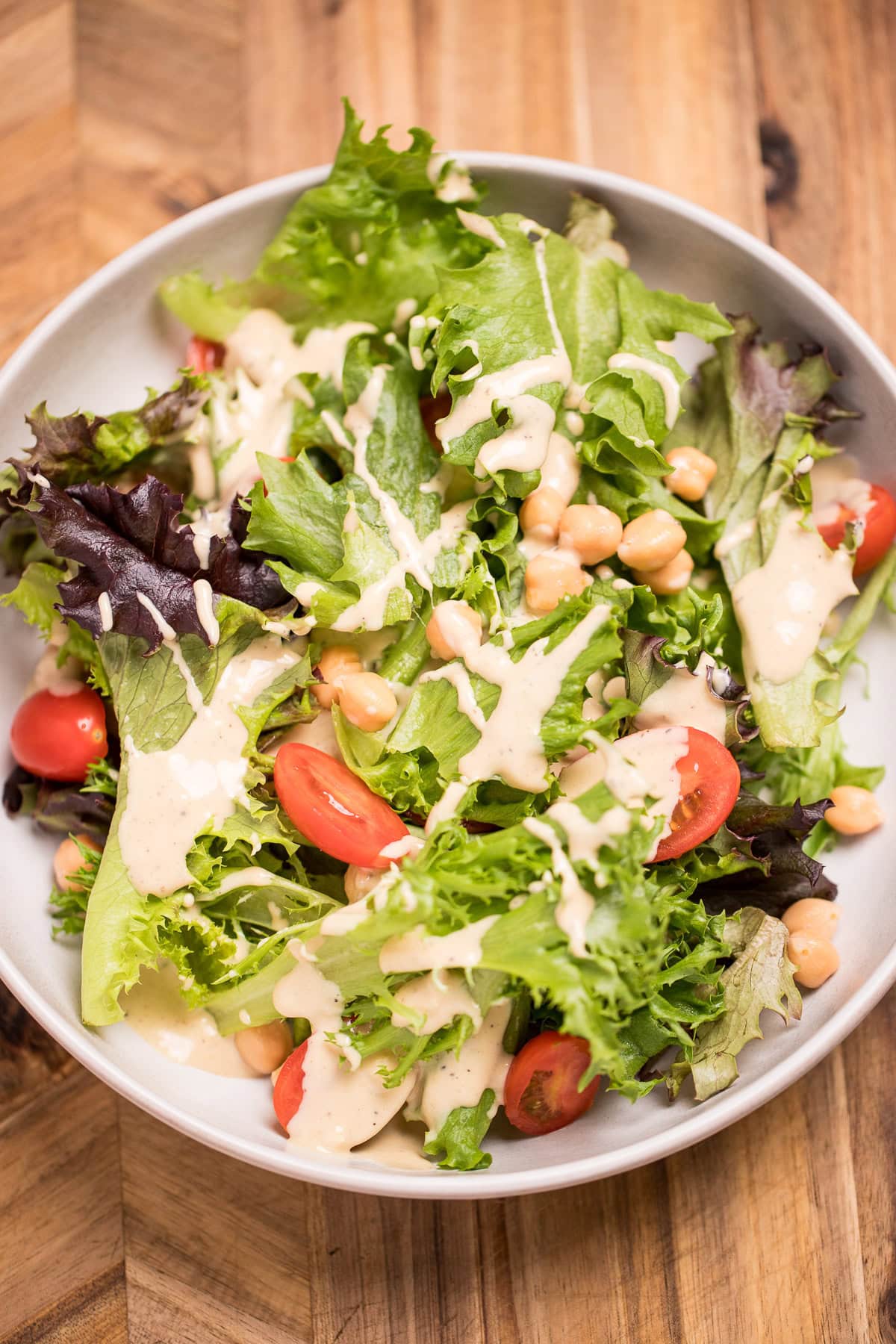 A salad with lettuce, cherry tomatoes, and chickpeas topped with lemon tahini dressing in a bowl on a cutting board.
