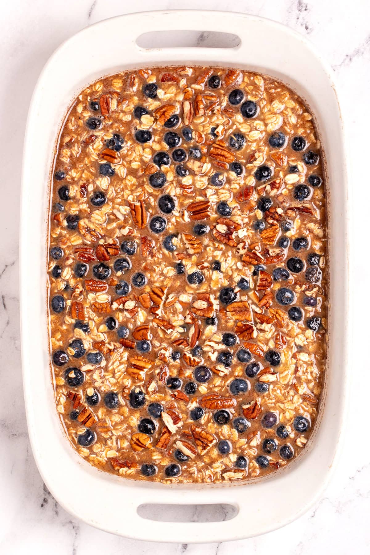 A baking dish with blueberry baked oatmeal before being cooked, on a table.