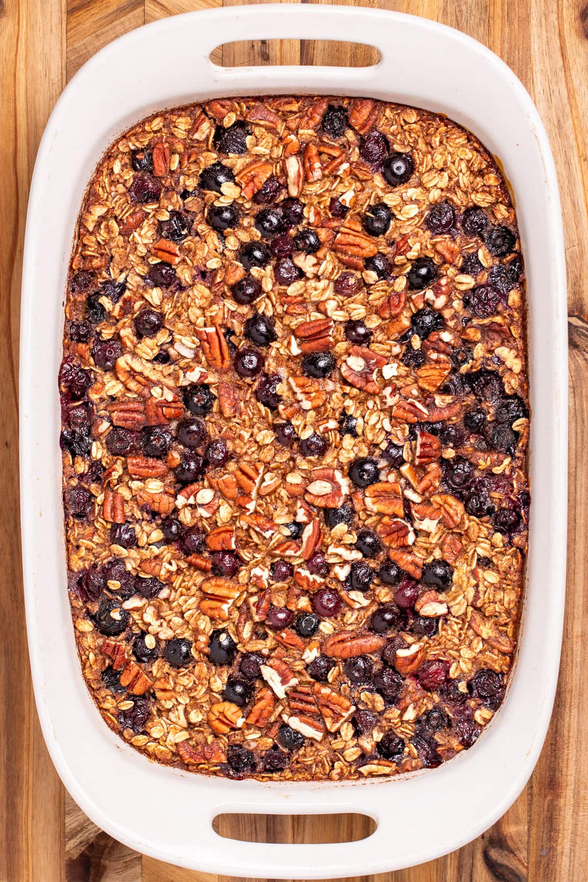 A baking dish with blueberry baked oatmeal, resting on a wooden cutting board.