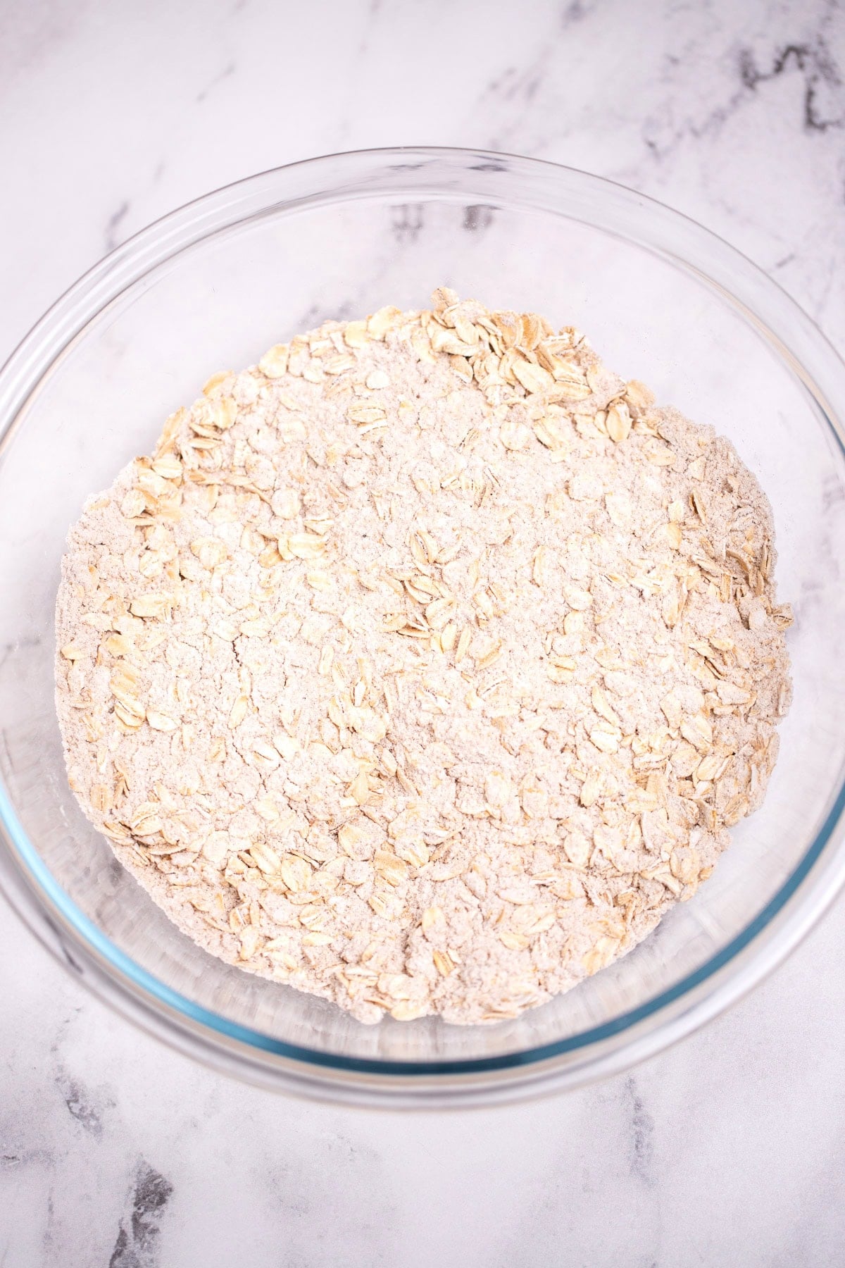 A glass bowl on a table full of oats mixed with brown sugar and gluten free flour.