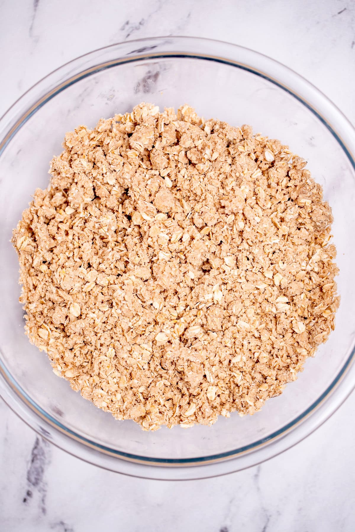 A glass bowl on a table with an oat crumble topping that was just mixed together.