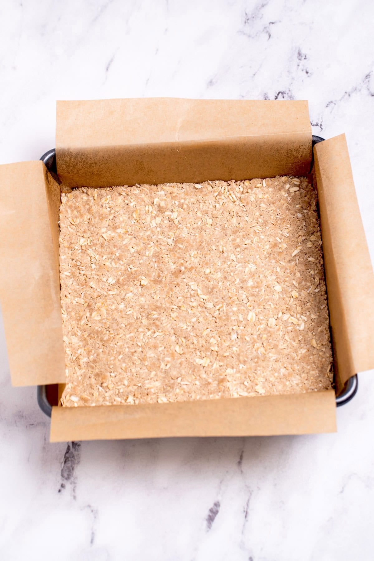 A baking pan lined with parchment paper with an oatmeal crust pushed into the bottom before baking.
